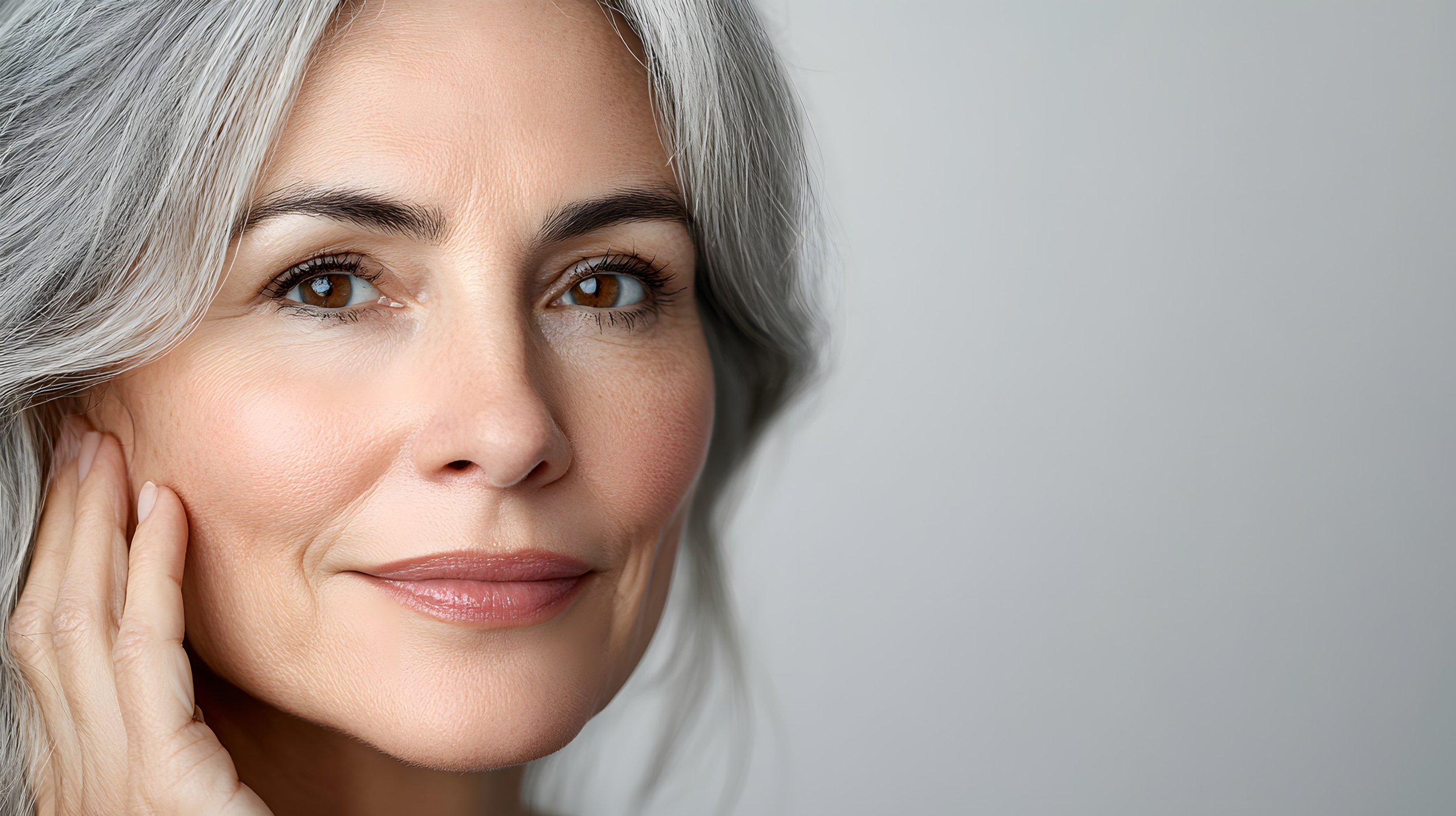 Close-up shot of a woman with grey hair looking in the camera against light, plain background