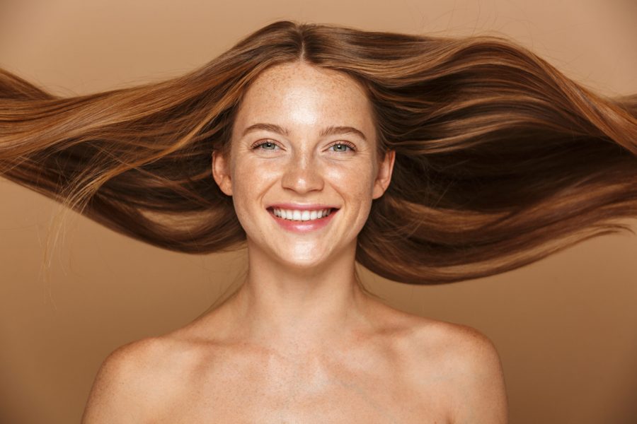 Beauty portrait of a beautiful healthy young topless woman with long red hair looking at camera isolated over beige background