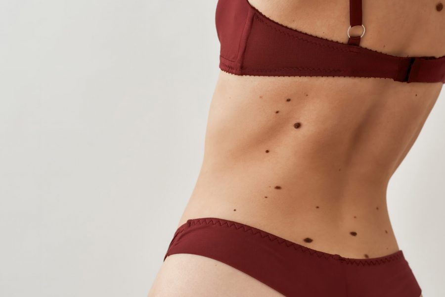 Closeup shot of back and buttocks of young caucasian woman in burgundy underwear standing isolated over light gray background. Vertical shot