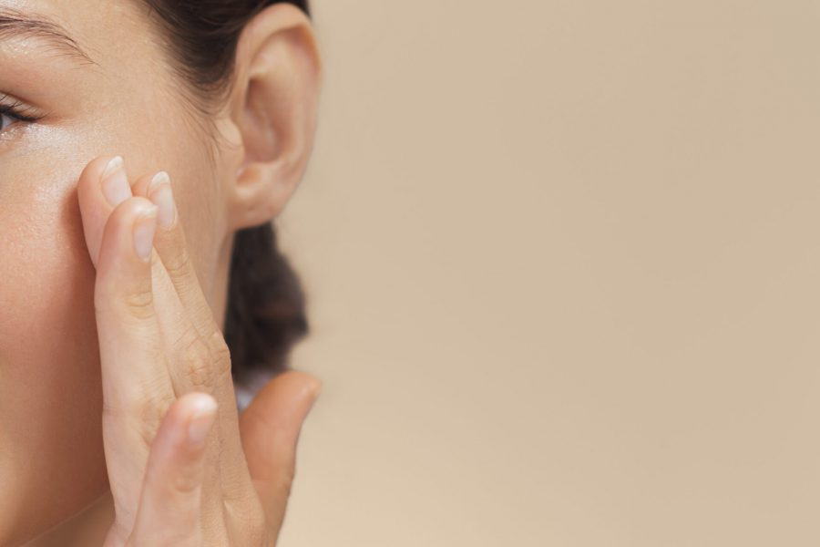 High-quality crop photo of skincare and cosmetics concept with copy space for text. Woman with beautiful face touching healthy facial skin portrait. Beautiful happy Asian girl model with natural makeup enjoys glowing hydrated skin