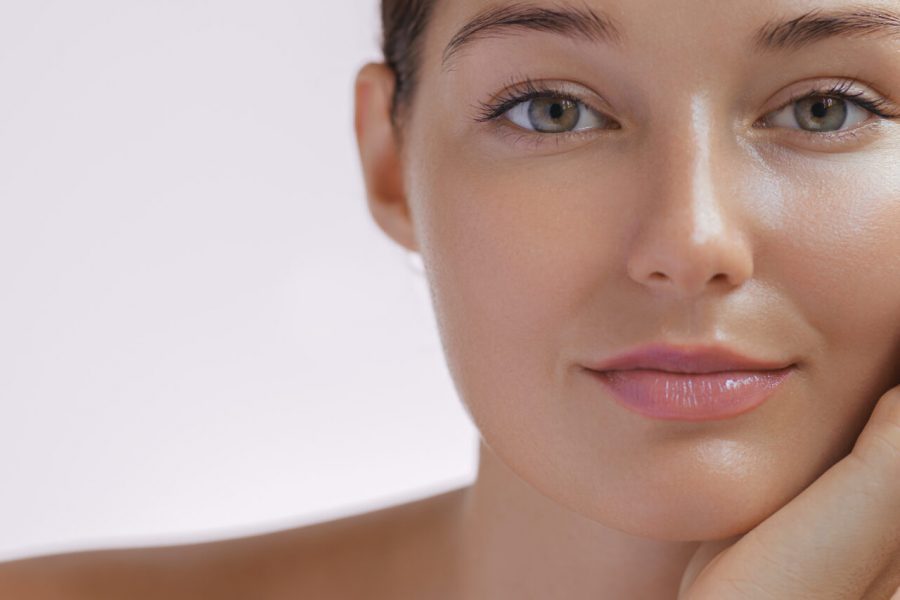 Skincare. Woman with beautiful face touching healthy facial skin. Fascinating portrait of confident girl model with natural makeup enjoys glowing hydrated skin on beige background closeup. High-quality photo